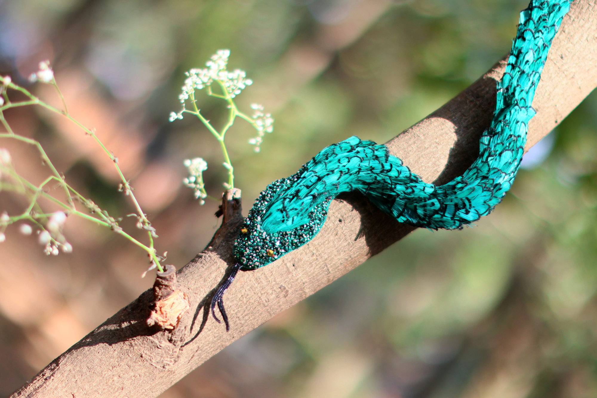 A hand embroidered hyper realistic snake handcrafted with crystals and feathers.